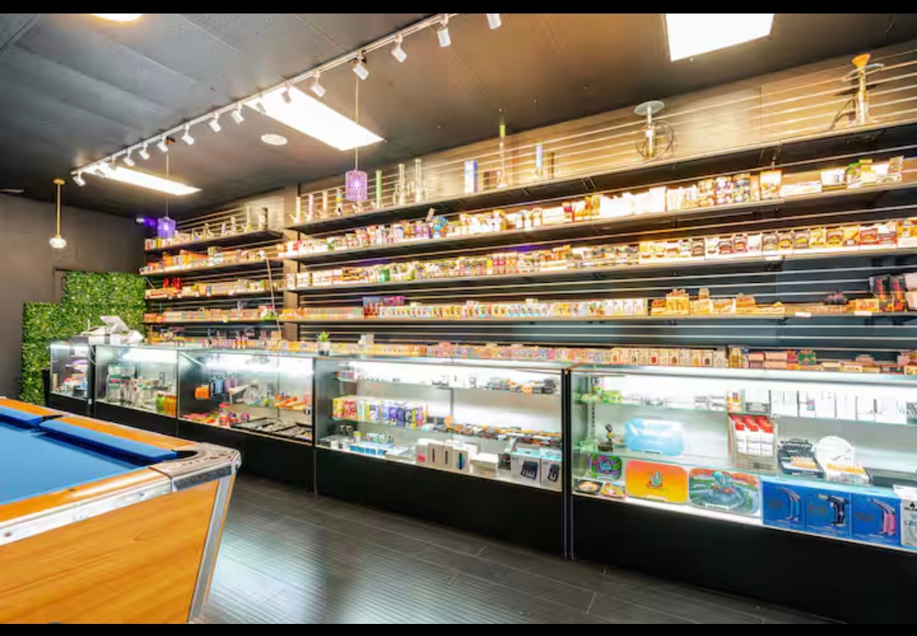 The counter run from the other end, with glass pieces and hookahs on the top shelves above rows of packaged product.