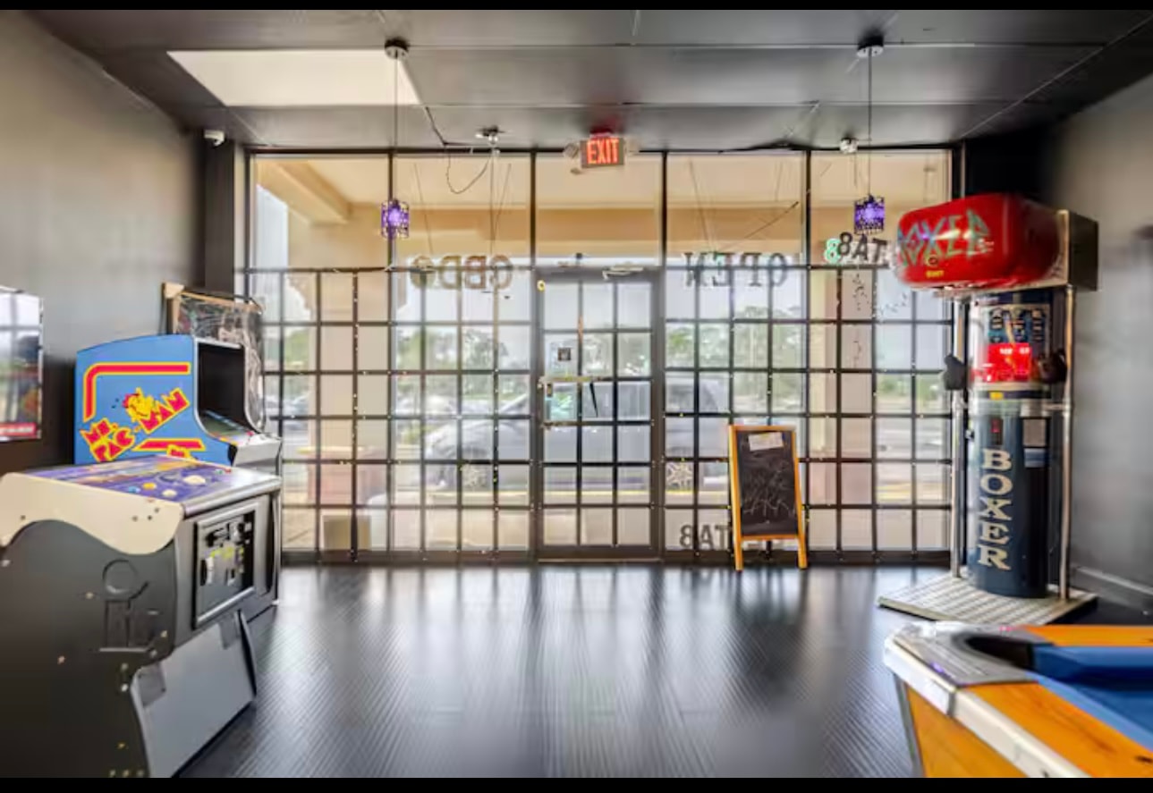 The arcade corner by the entrance: a Ms. Pac-Man cabinet and a Boxer machine flanking the front windows.