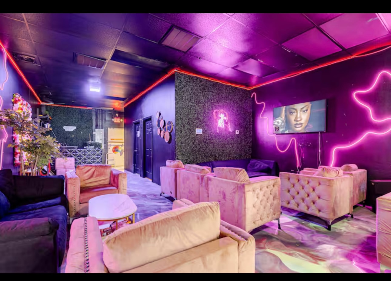 Lounge seating arranged around a hedge-panelled wall under pink neon.